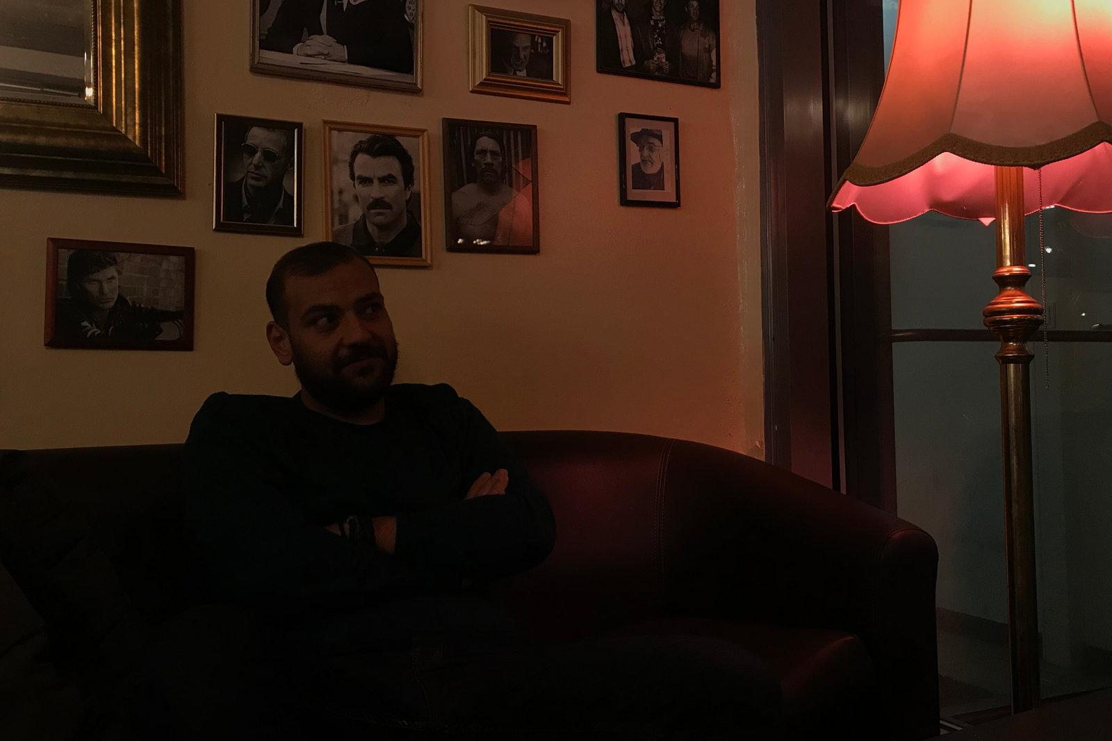 Mostafa Bastami sitting on a leather sofa under framed film portraits, lit by a red lamp